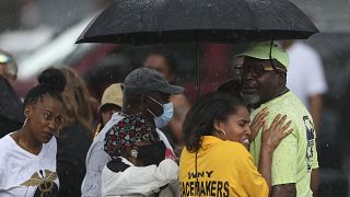 Bystanders gather under an umbrella as rain rolls in after a shooting at a supermarket on Saturday, May 14, 2022, in Buffalo, N.Y.