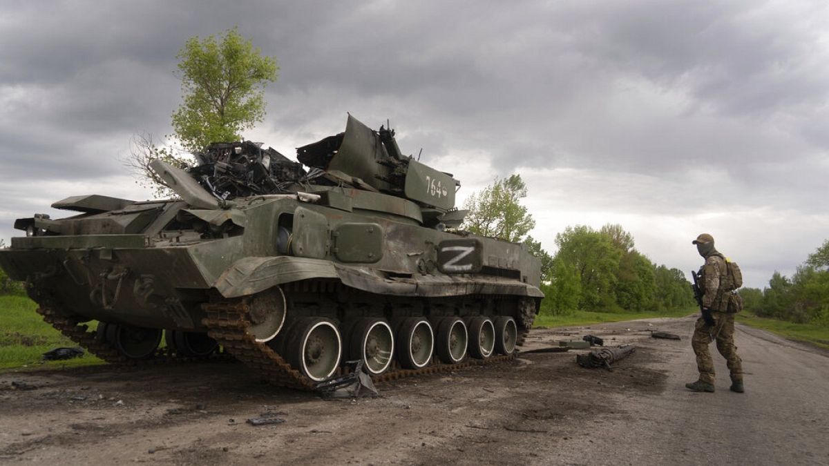 ukrán katona egy elpusztított orosz harcjármű mellett