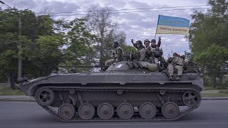 Ukrainian serviceman wave a flag with writing reading in Ukrainian "Glory to Ukraine", top, and "Death to the enemies" as they ride atop a tank in the Kharkiv region on 16 Ma