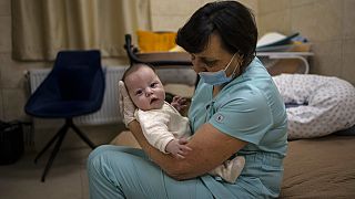 Újszülöttel játszik egy nővér a kijevi klinika óvóhelyén, 2022 március 19-én