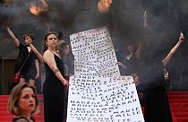 "Les Colleuses" hold a banner with names of 129 women who died in the last 12 months