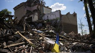Ukrán zászló egy lebombázott épület mellett 2022. május