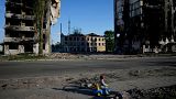 پسری در مقابل خانه‌های ویران شده در بورودیانکا، اوکراین دوچرخه سواری می‌کند