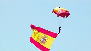 Un paracaidista desciende con la bandera española en el desfile del Día de las Fuerzas Armadas