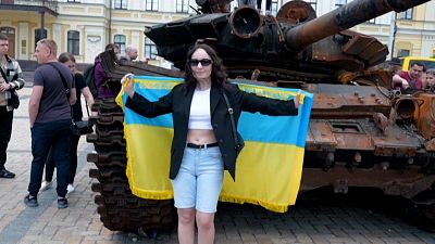 Woman with Ukrainian flag near destroyed russian tank.