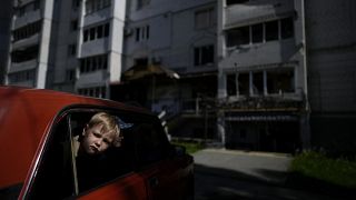Kinder in einem Auto vor einem durch Angriffe zerstörten Gebäude in Borodjanka, am Stadtrand von Kiew (31. Mai 2022)