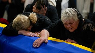 The mother, right, and sister of Army Col. Oleksander Makhachek mourn over the coffin with his remains during a funeral service in Zhytomyr, Ukraine, Friday, June 3, 2022.