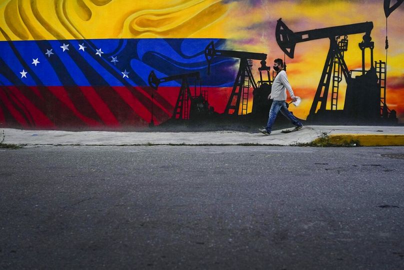 A man walks past a mural featuring oil pumps and wells in Caracas, Venezuela