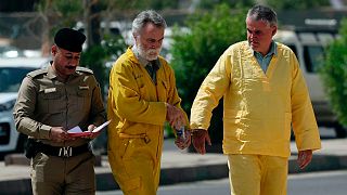 Jim Fitton, centre, and Volker Waldmann, right, are handcuffed as they walk to a courtroom escorted by police arriving to court in Baghdad, Iraq, Sunday, May 22, 2022.