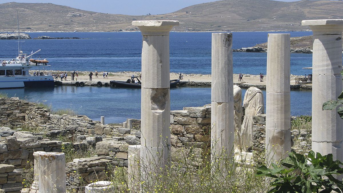 Antiguas estatuas y columnas de una casa milenaria encima del muelle de desembarco en el parque arqueológico de Delos, Grecia, el 25 de mayo de 2019
