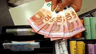 Euro coins and banknotes are shown by a salesclerk at a shop in Vilnius, Lithuania. 