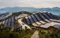 Un grupo de personas pasa por delante de los paneles solares de una central fotovoltaica en el condado de Songxi, en la provincia de Fujian, en el sureste de China.