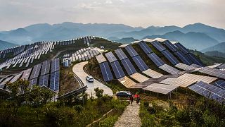 Des personnes marchent devant des panneaux solaires dans une centrale photovoltaïque du comté de Songxi, dans la province de Fujian (sud-est de la Chine)