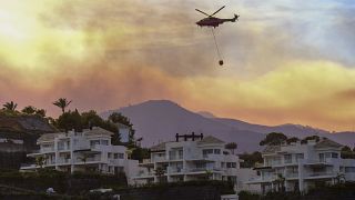 Un helicóptero lleva agua sobre un incendio forestal avanza cerca de propiedades en Marbella, Málaga, el jueves 9 de junio de 2022.