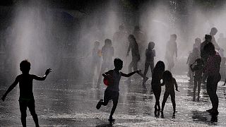 Children and adults cool off in a fountain in a park by the river in Madrid, Spain, Sunday, June 12, 2022.