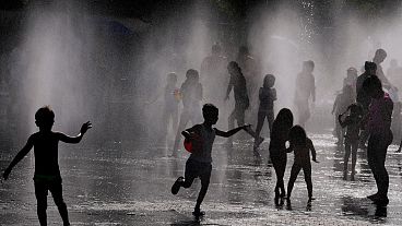 Children and adults cool off in a fountain in a park by the river in Madrid, Spain, Sunday, June 12, 2022.