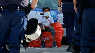 A boy looks at policemen as he waits to enter a bus from Kara Tepe refugee camp on Lesbos, 28 September 2020