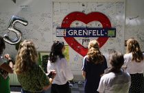 People observe the memorial, near to the remains of the Grenfell Tower.