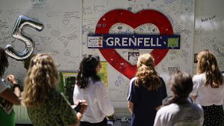 People observe the memorial, near to the remains of the Grenfell Tower.