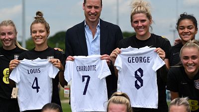 Prince William holding the England football jersey bearing the names of his three children and with the England women football team