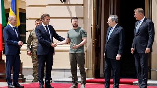 Emmanuel Macron aperta a mão a Volodymyr Zelenskyy perante o olhar de Olaf Scholz, Mario Draghi e Klaus Iohannis