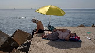 A woman sleeps under an umbrella on a breakwater in front of the Mediterranean Sea in Barcelona, Spain, 16 June 2022.
