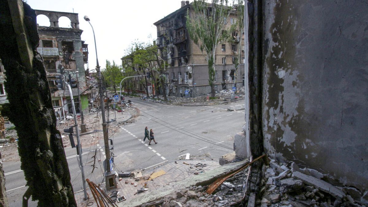 People walk among buildings destroyed during fighting in Mariupol