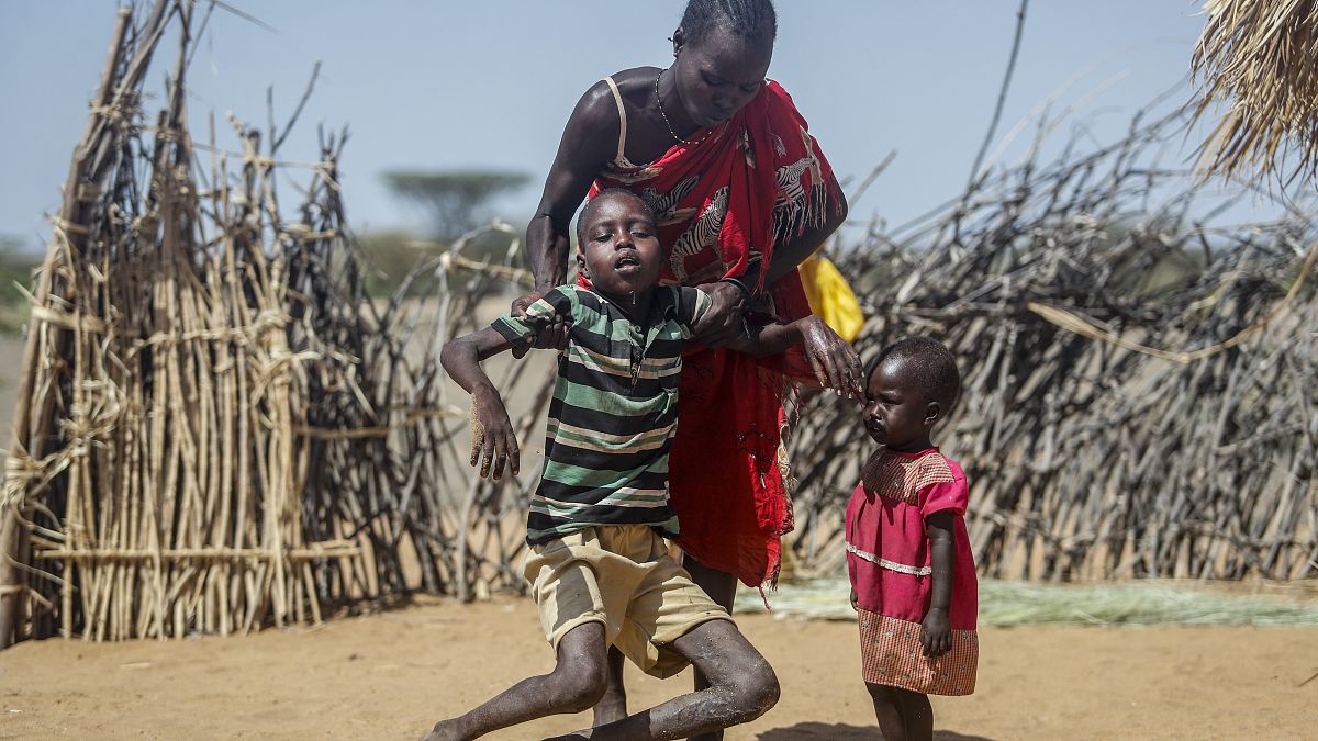 أم تساعد ابنها المصاب بسوء التغذية على الوقوف بعد أن انهار بالقرب من كوخهم في قرية لوموبوث في شمال كينيا. 2022/05/12