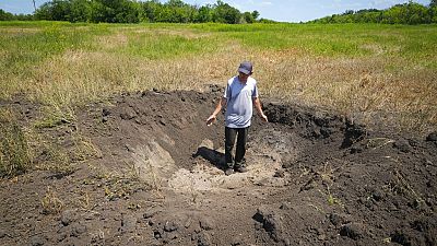 Local grain producer, shows a crater left by a Russian shell on his field