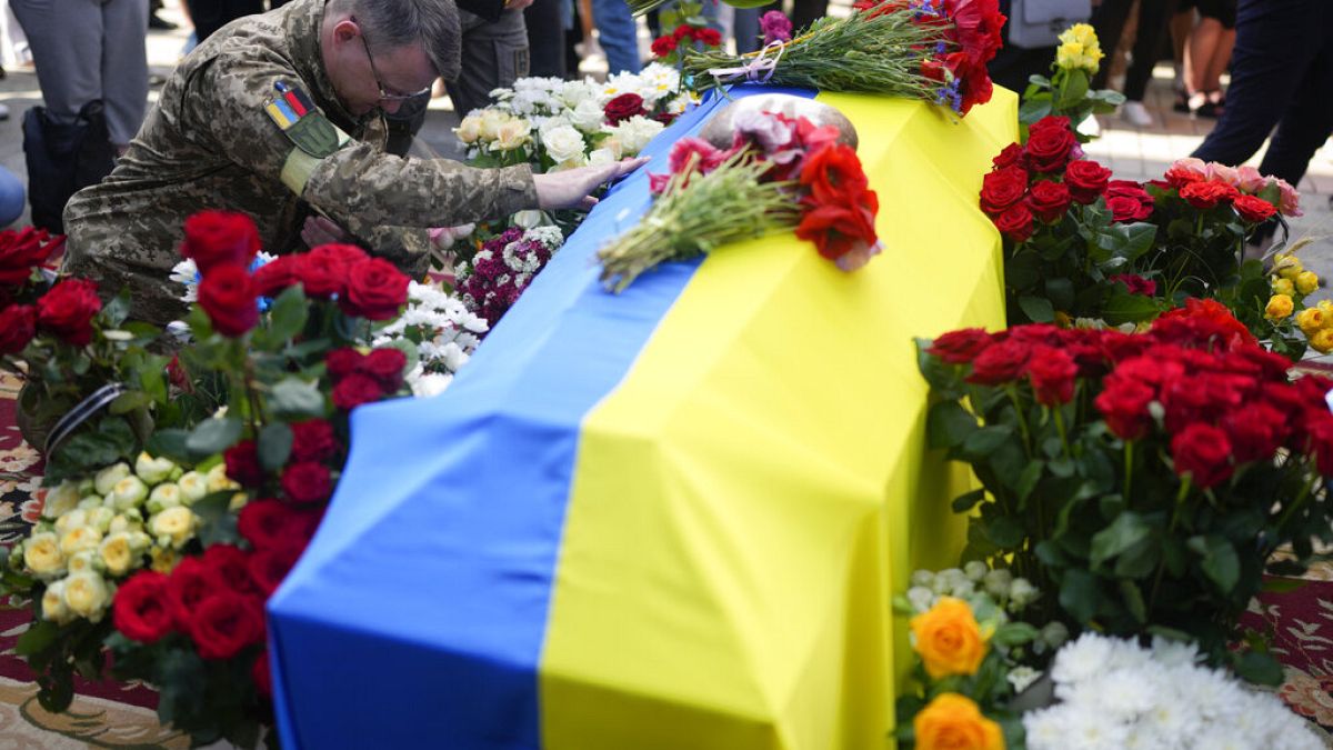 A solider kneels at activist and soldier Roman Ratushnyi's coffin during the memorial service in Kyiv, Ukraine, June 18, 2022