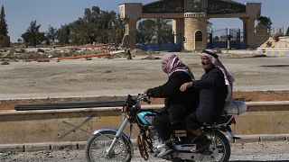 راكبان على دراجة نارية مقابل مدرسة سابقة كانت تابعة لتنظيم الدولة الإسلامية في الرقة