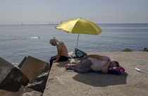 Una mujer duerme bajo una sombrilla en un rompeolas frente al mar Mediterráneo en Barcelona, España, el jueves 16 de junio de 2022.