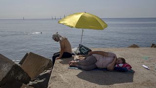 Una mujer duerme bajo una sombrilla en un rompeolas frente al mar Mediterráneo en Barcelona, España, el jueves 16 de junio de 2022.