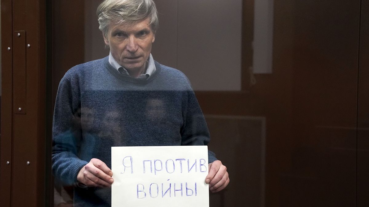 Alexei Gorinov holds a sign "I am against the war" standing in a cage during hearing in the courtroom in Moscow, Russia, Tuesday, June 21, 2022.