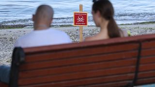 Пара сидит на скамейке на пляже с надписью «Опасно! Мины!» в черноморском украинском городе Одессе,  13 июня 2022 года.