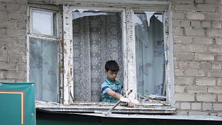 Мальчик убирает осколки разбитого оконного стекла после обстрела города Бахмут в Донецкой области