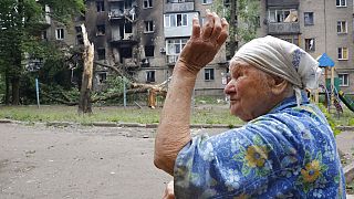 Idős hölgy, a háttérben lebombázott házakkal