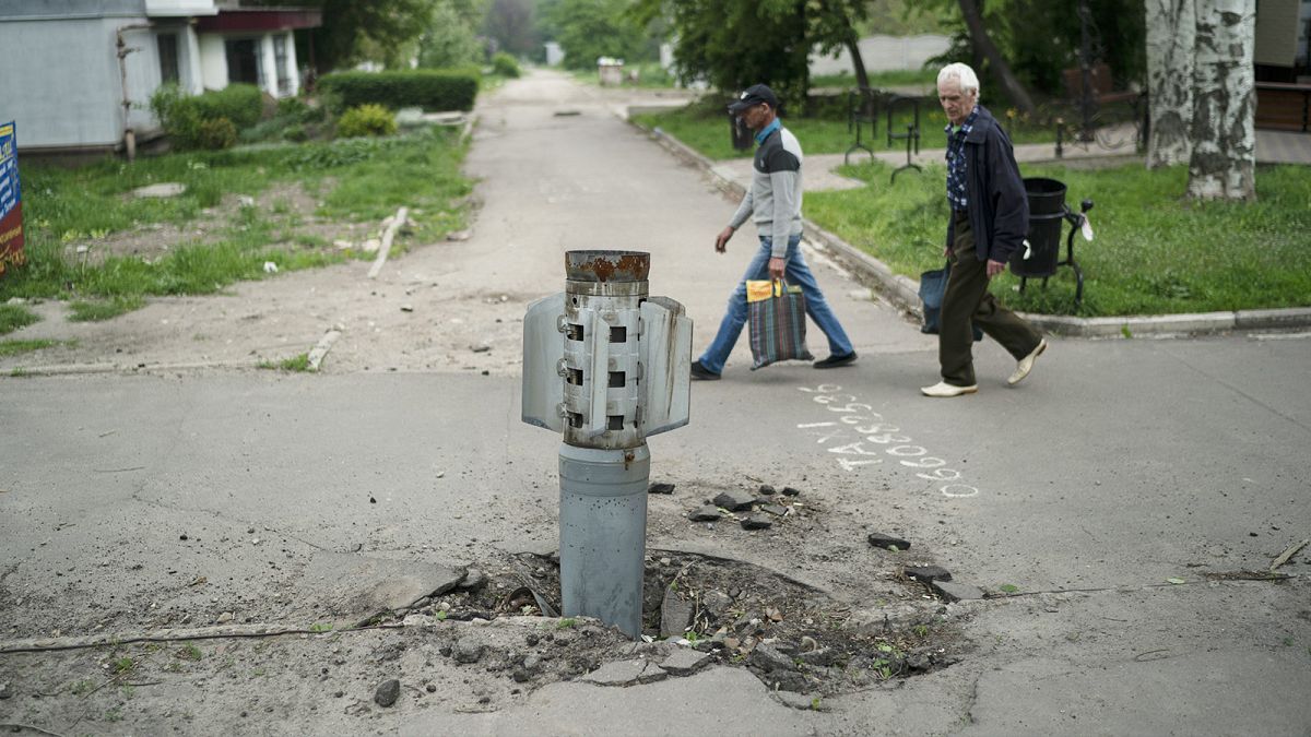 People walk past part of a rocket that sits wedged in the ground in Lysychansk, 19 May 2022
