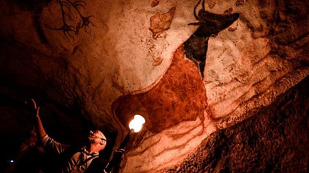 An employee shows paintings inside the life size Lascaux cave replica during a special immersive torch light visit on June 16, 2022 in Montignac.
