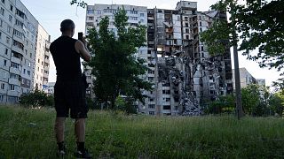 یک شهروند اوکراینی در حال گرفتن عکس از ویرانه‌های یک ساختمان در شهر خارکیف به تاریخ یک ژوئیه ۲۰۲۲