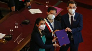 El presidente de Chile, Gabriel Boric, en el centro, sostiene el borrador final de una propuesta de nueva constitución