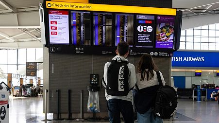 A couple looks at an electronic flight information board at Terminal 5 of London’s Heathrow Airport.