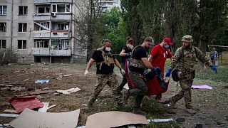 Paramedics carry the body of a woman who was killed during a Russian bombardment at a residential neighborhood in Kharkiv, Ukraine, on Thursday, July 7, 2022.