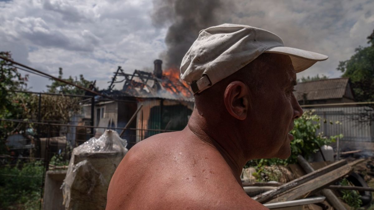 A man looks at damages as smoke rises from a house caught on fire, after cluster rockets hit a residential area, in Konstantinovka, eastern Ukraine, Saturday, July 9, 2022.