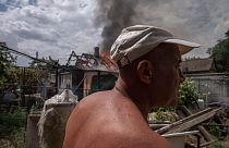 A man looks at damages as smoke rises from a house caught on fire, after cluster rockets hit a residential area, in Konstantinovka, eastern Ukraine, Saturday, July 9, 2022.
