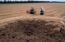 A crater left by a Russian rocket attack is seen as a farmer collects harvest in a field that is ten kilometres away from the frontline, July 4, 2022.