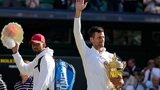 Serbia's Novak Djokovic (R) holds the winner's trophy as he celebrates after beating Australia's Nick Kyrgios (L) to win the men's singles final at Wimbledon, July 10, 2022.