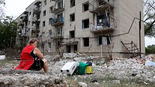 Moradora sentada ao lado dos seus pertences junto ao prédio que foi bombardeado em Chasiv Yar, leste da Ucrânia