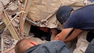 Serviceman giving first aid to survivor under rubble of destroyed apartment building