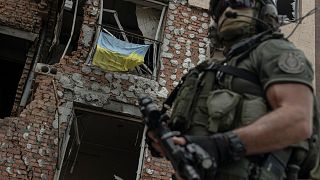 A Ukrainian serviceman is backdropped by a destroyed building in Irpin, Ukraine, Monday, July 11, 2022.